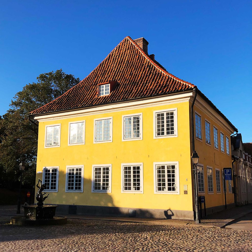 Gult stenhus med fönster bestående av många små fönsterrutor. Framför huset syns skulpturen Sjöjungfrun.