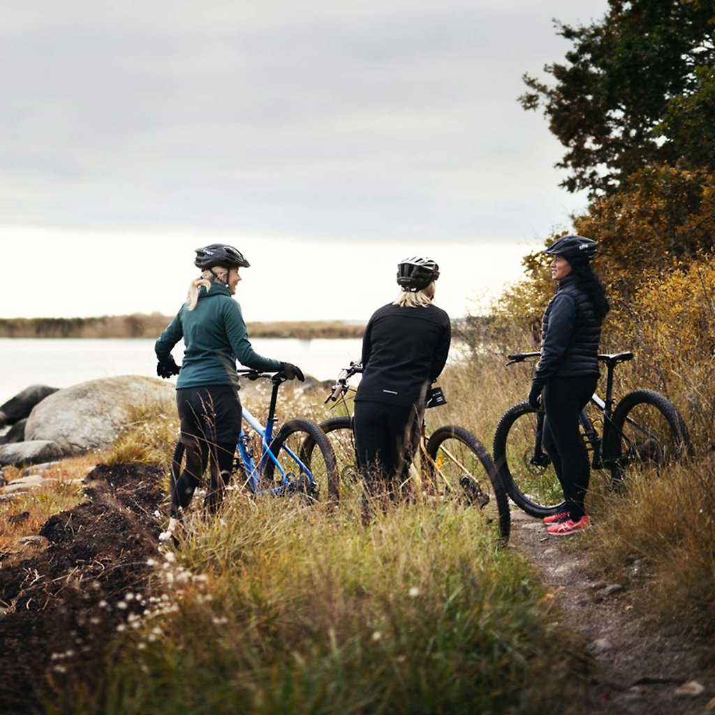 Three women standing with their bikes on a path close to the water. 